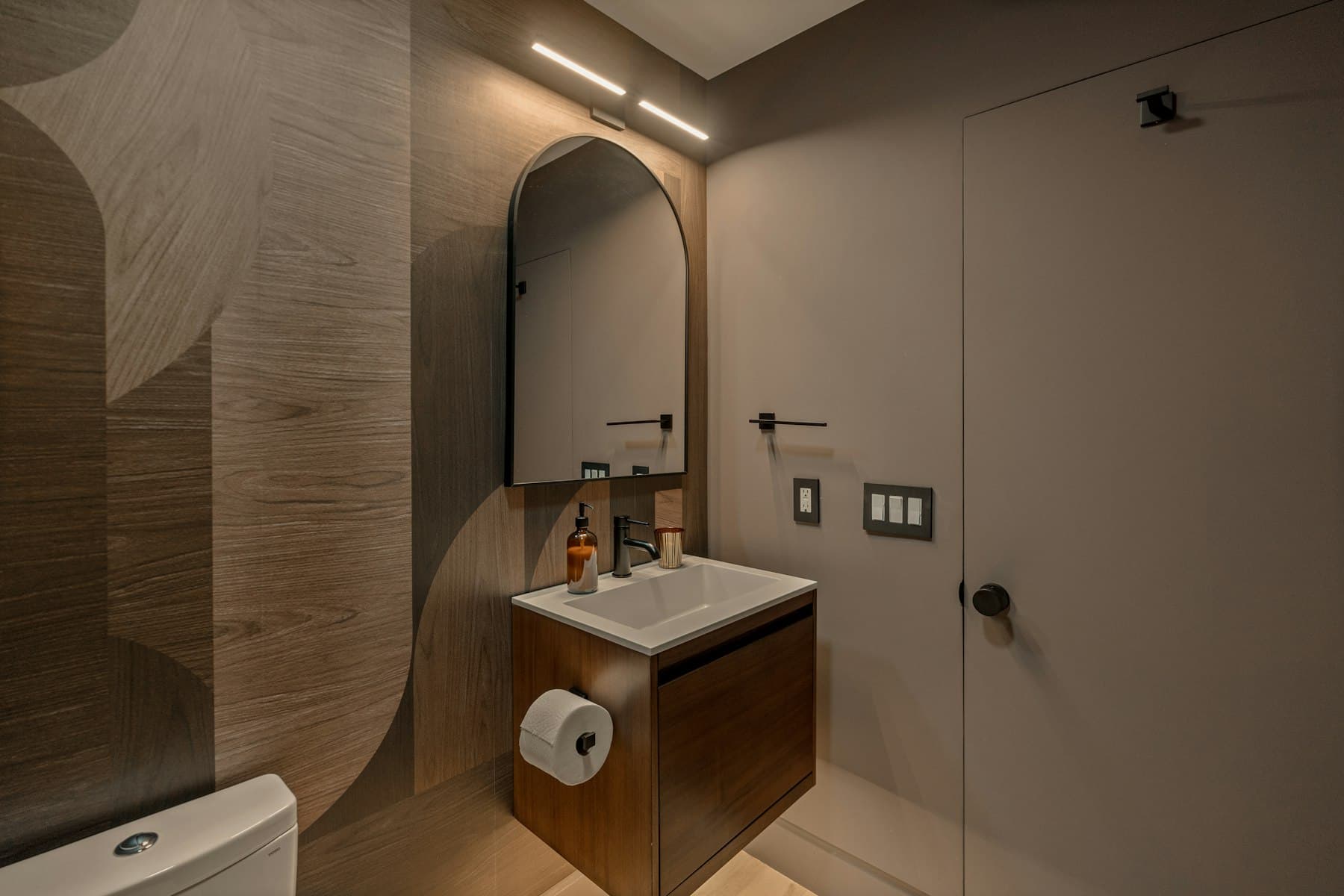 Bathroom with a wall-hung wooden vanity, arched mirror and textured walls