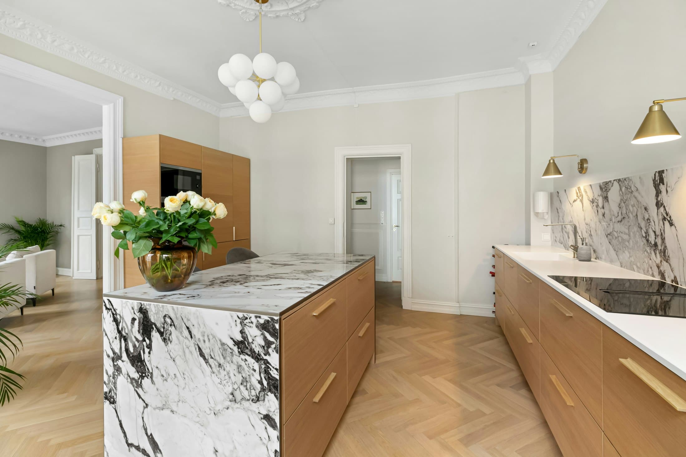 Marble-topped kitchen island beside tall wooden cabinets and a bright window