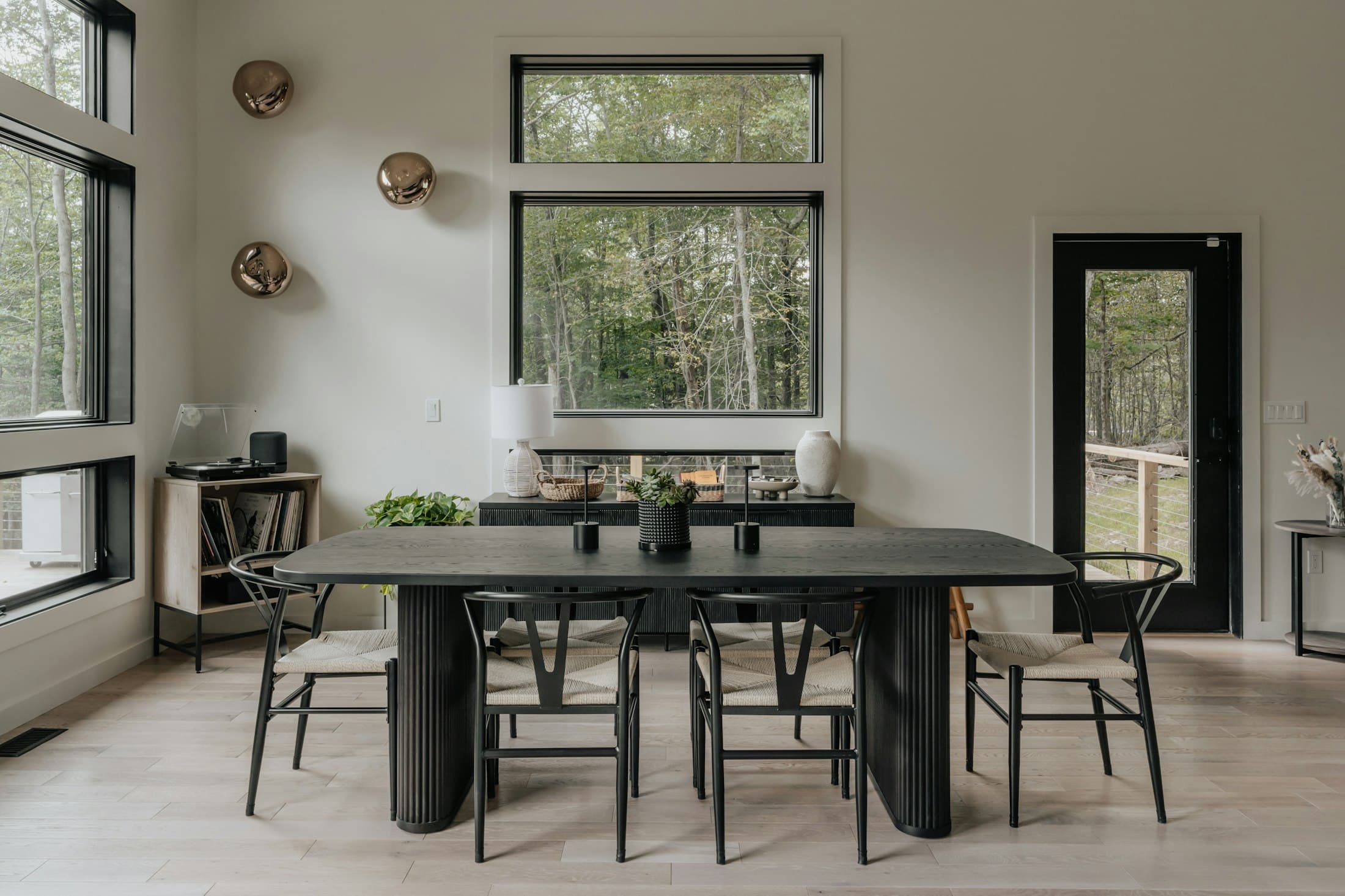Dining area with a long dark table and large windows overlooking trees